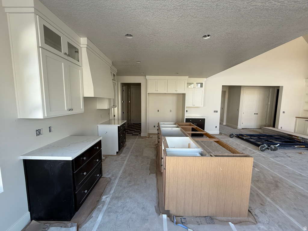 Kitchen featuring a kitchen island, glass insert cabinets, white cabinets, dark cabinetry, and a textured ceiling
