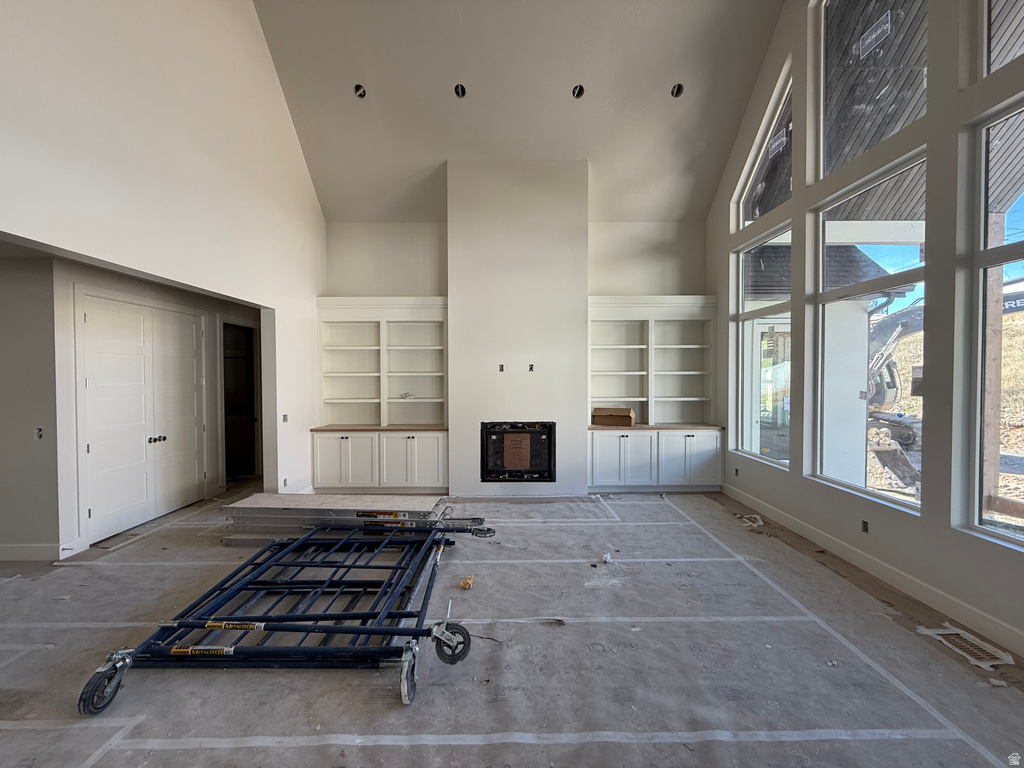 Unfurnished living room featuring high vaulted ceiling and a glass covered fireplace