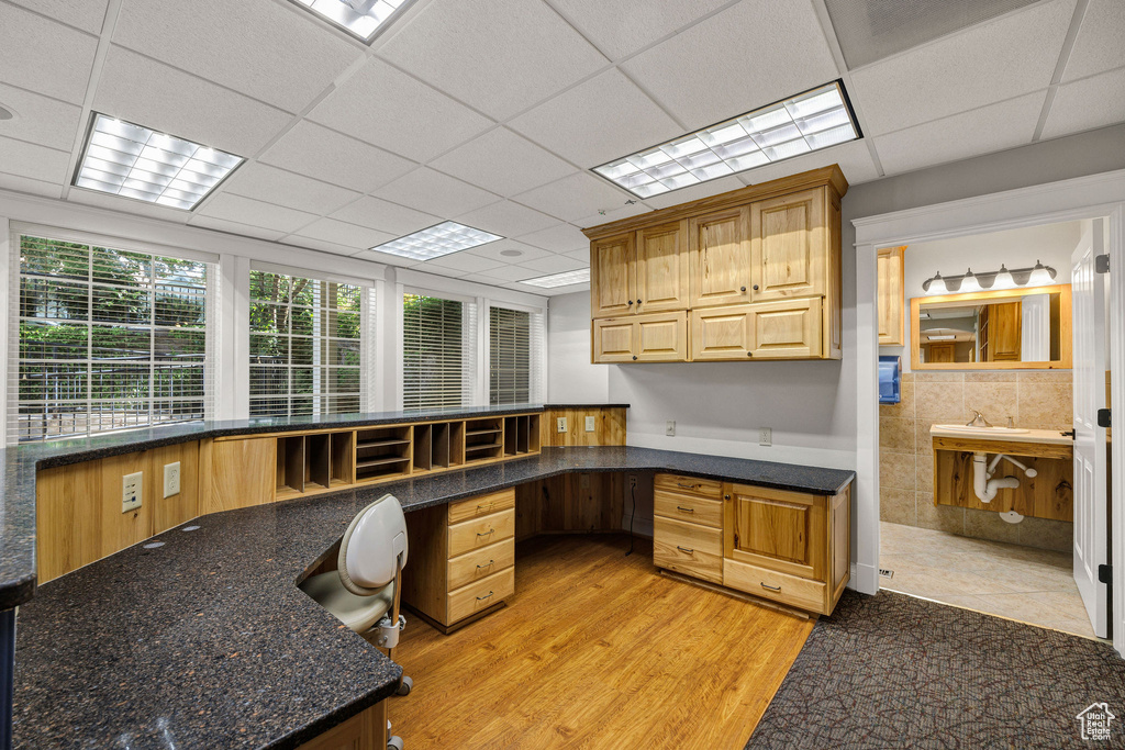 Home office with built in desk, light wood-type flooring, and a drop ceiling