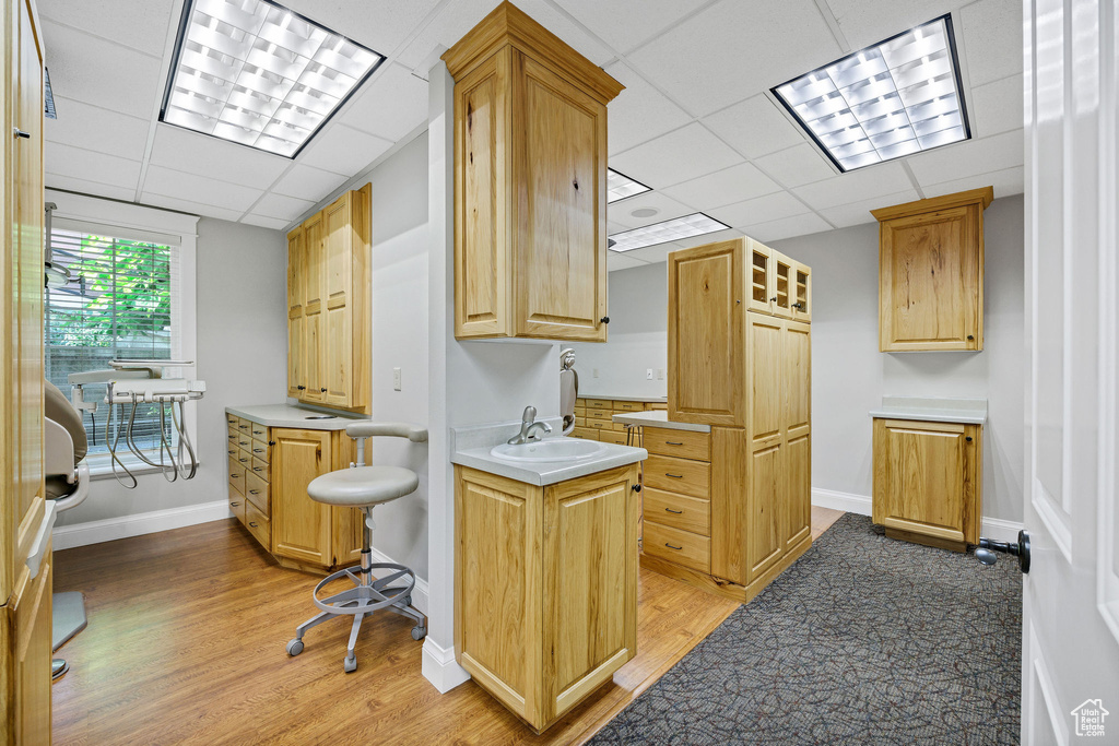 Kitchen featuring light countertops, light wood finished floors, a paneled ceiling, and glass insert cabinets