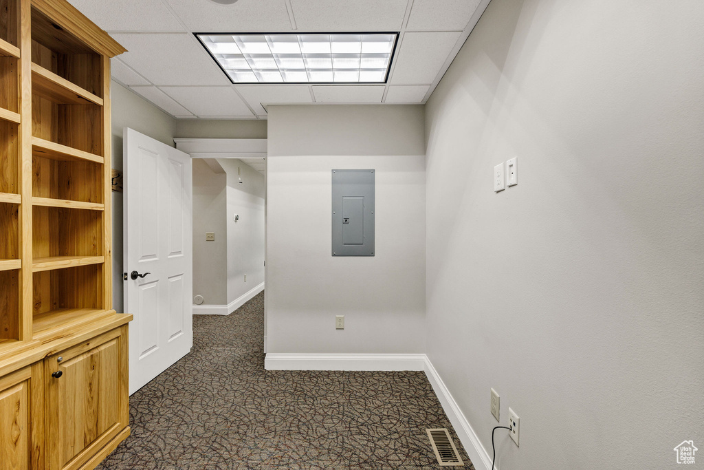 Corridor with a paneled ceiling, dark colored carpet, and electric panel