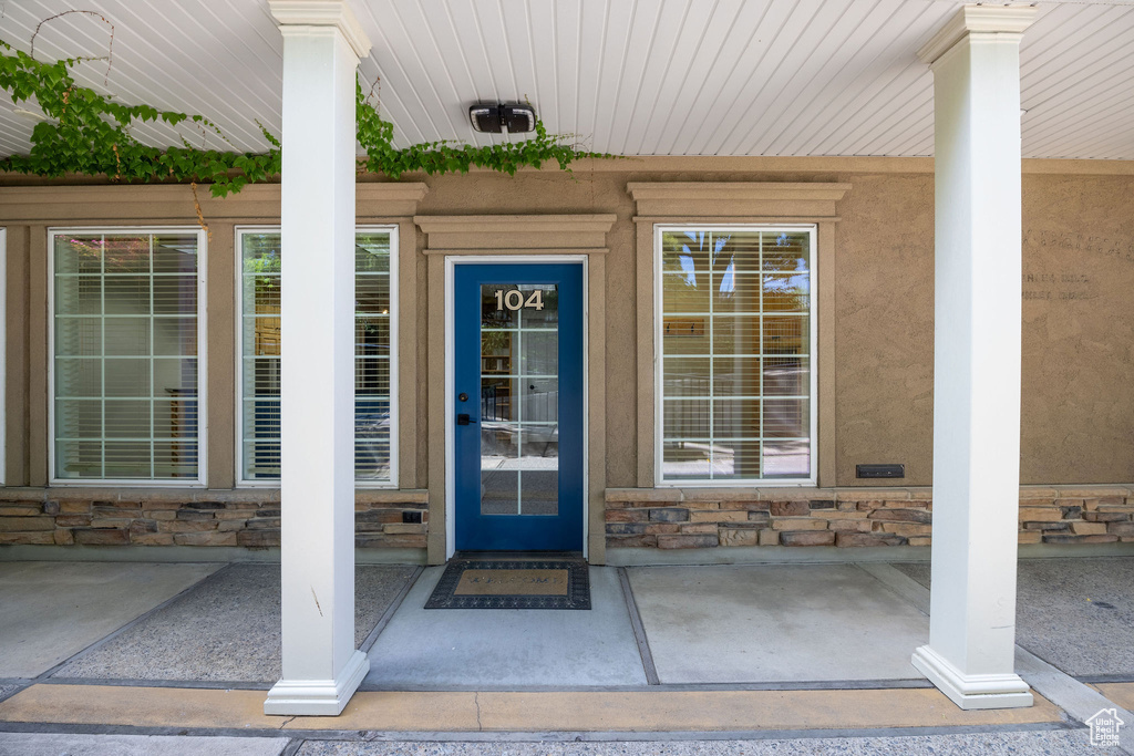 Doorway to property featuring stone siding, a porch, and stucco siding