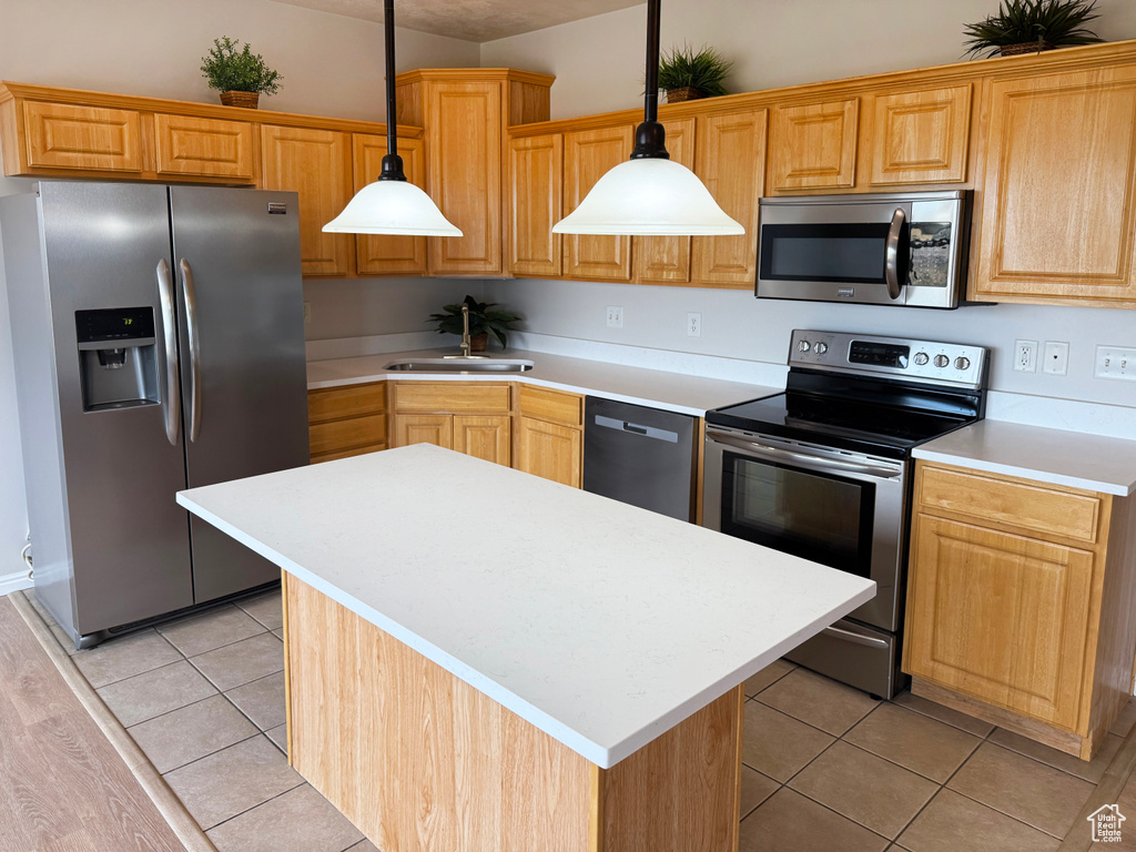 Kitchen featuring stainless steel appliances, light countertops, a kitchen island, light tile patterned floors, and pendant lighting