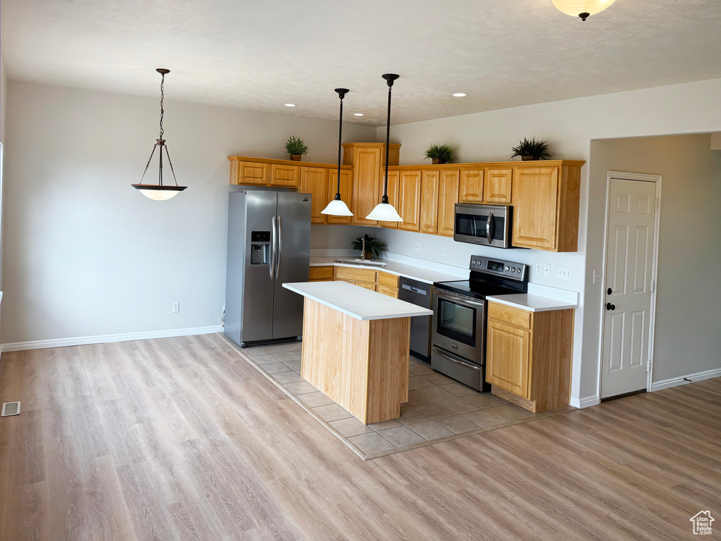 Kitchen with stainless steel appliances, a kitchen island, light countertops, light wood finished floors, and decorative light fixtures
