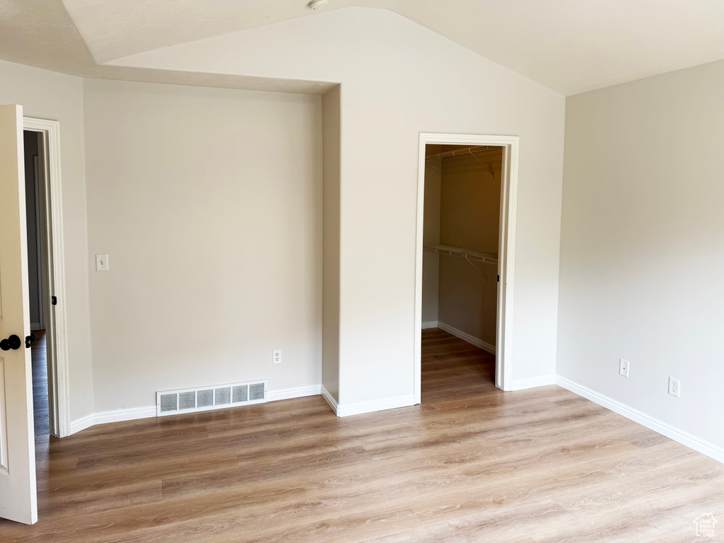 Unfurnished bedroom featuring a spacious closet, light wood-style flooring, and lofted ceiling