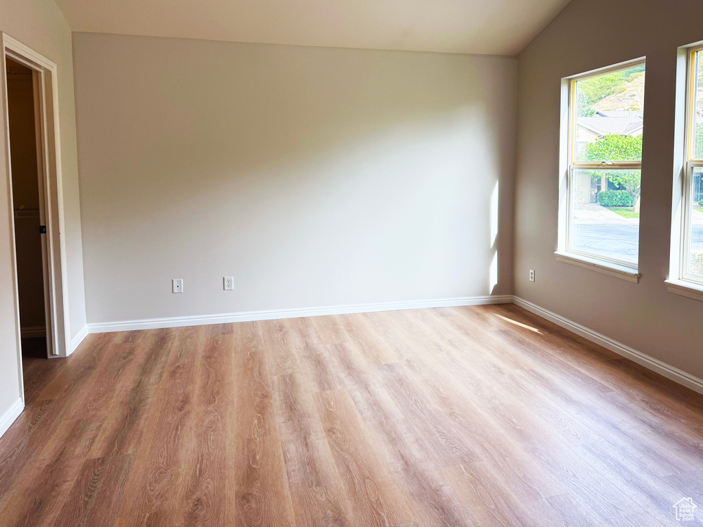 Empty room with vaulted ceiling and light wood-style floors