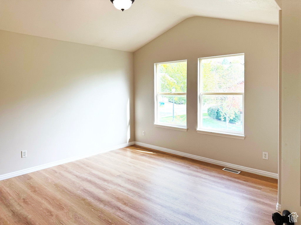 Spare room featuring light wood finished floors and vaulted ceiling