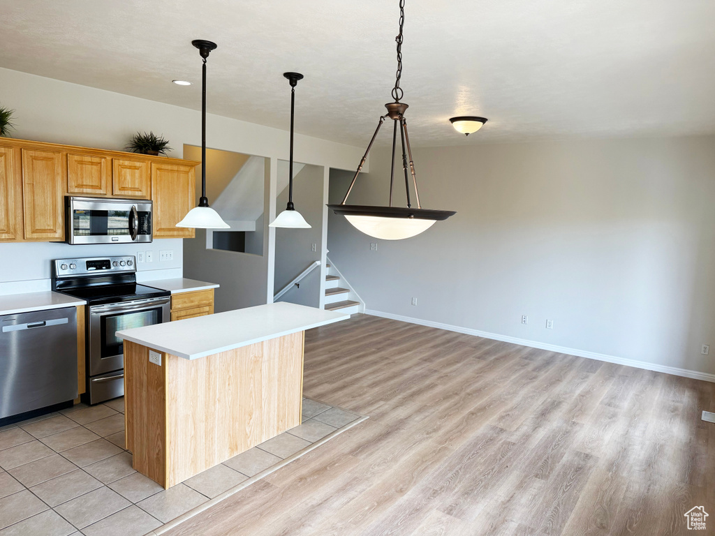 Kitchen with stainless steel appliances, a kitchen island, light countertops, pendant lighting, and light wood-type flooring
