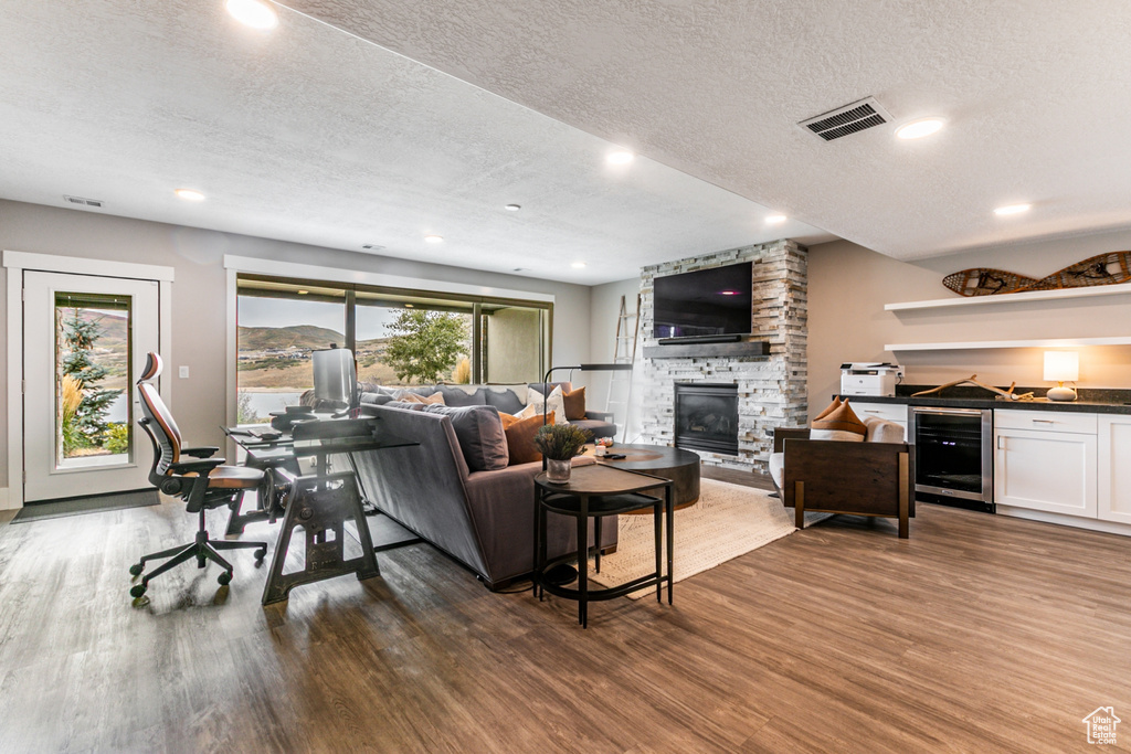 Living area featuring a textured ceiling, beverage cooler, a fireplace, wood finished floors, and recessed lighting