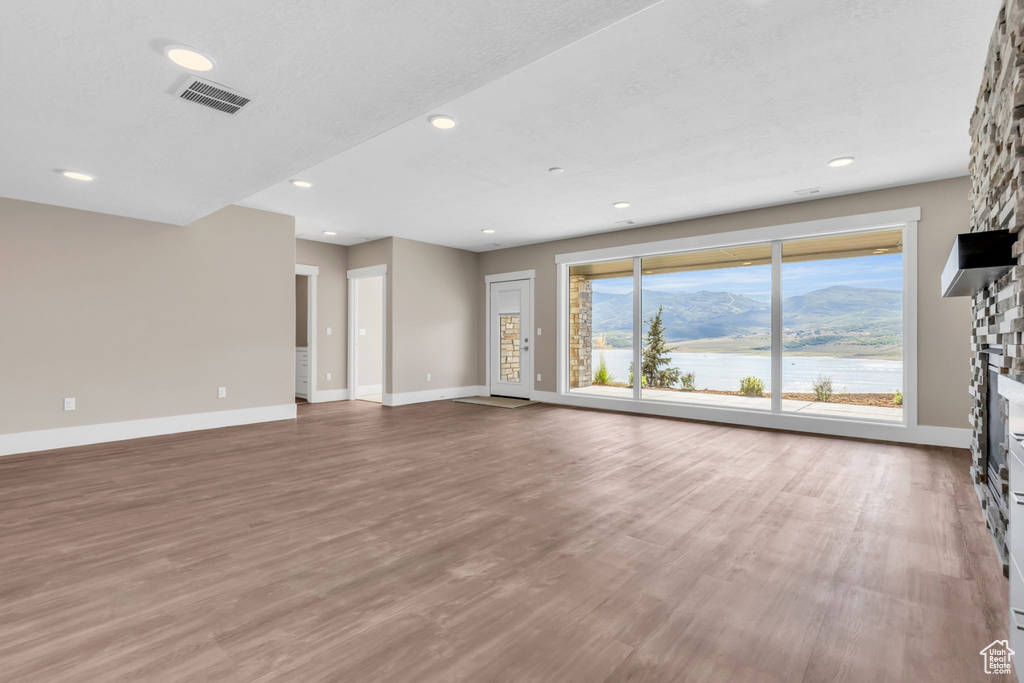 Unfurnished living room with a water and mountain view, a fireplace, light wood-type flooring, and recessed lighting