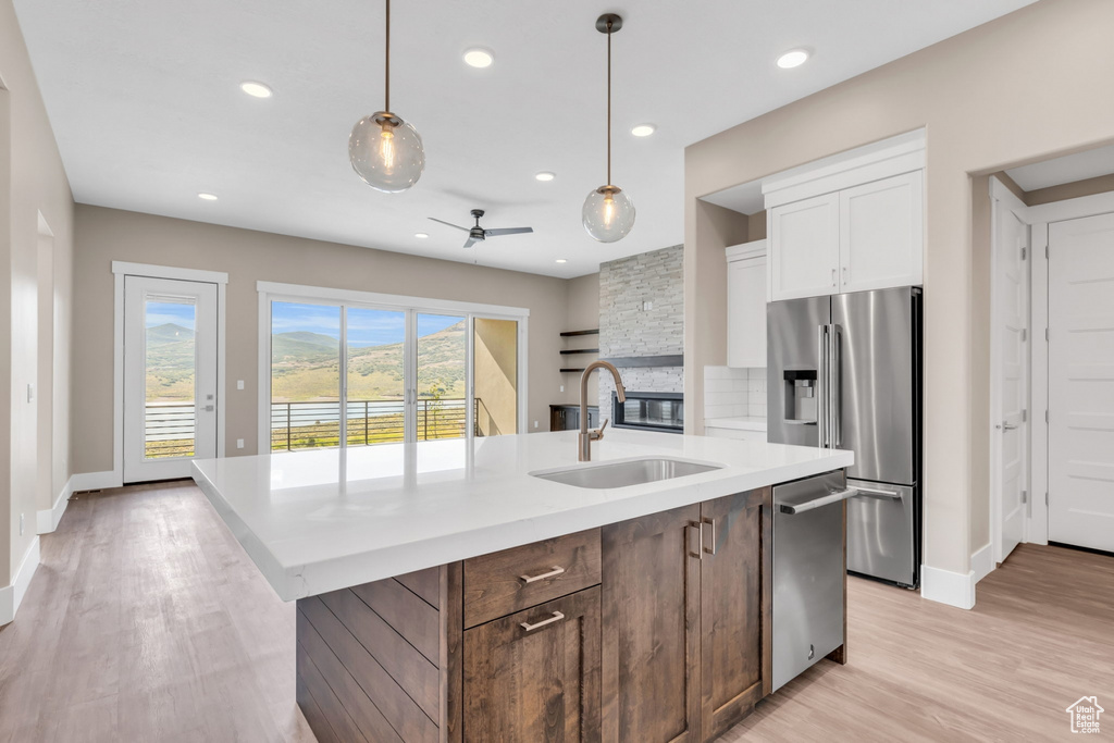 Kitchen with a kitchen island with sink, white cabinetry, decorative light fixtures, stainless steel appliances, and ceiling fan