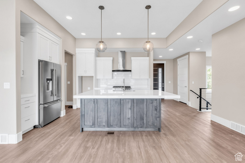 Kitchen with decorative light fixtures, appliances with stainless steel finishes, an island with sink, white cabinets, and light wood-style flooring
