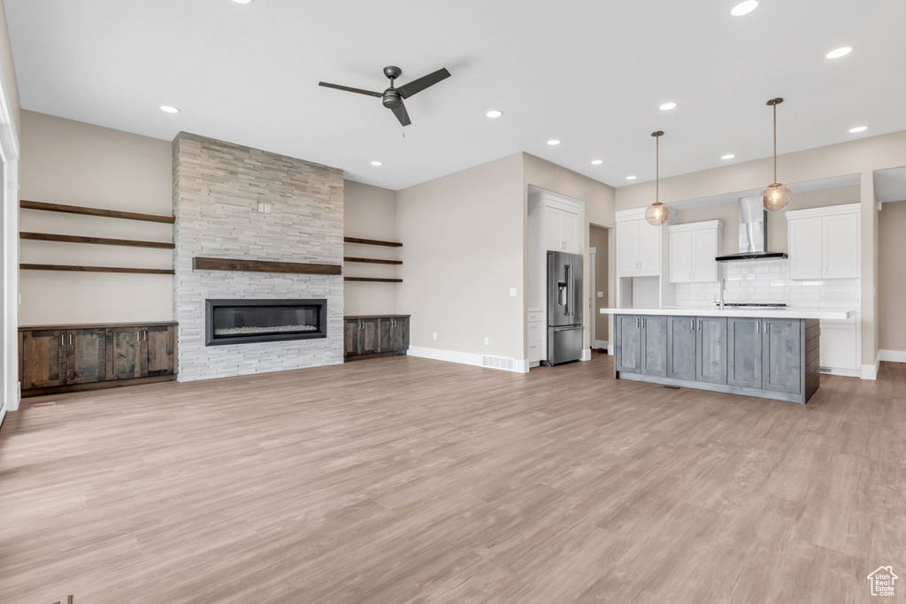 Unfurnished living room featuring light wood-style flooring, ceiling fan, a stone fireplace, and recessed lighting