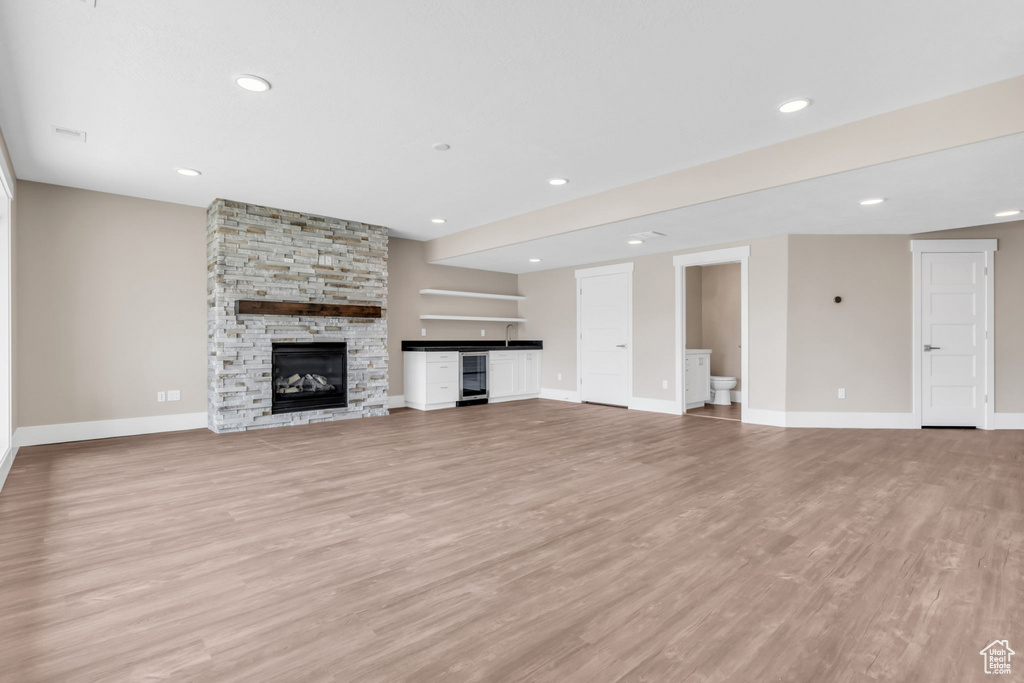 Unfurnished living room featuring a stone fireplace, light wood-style flooring, recessed lighting, and wine cooler
