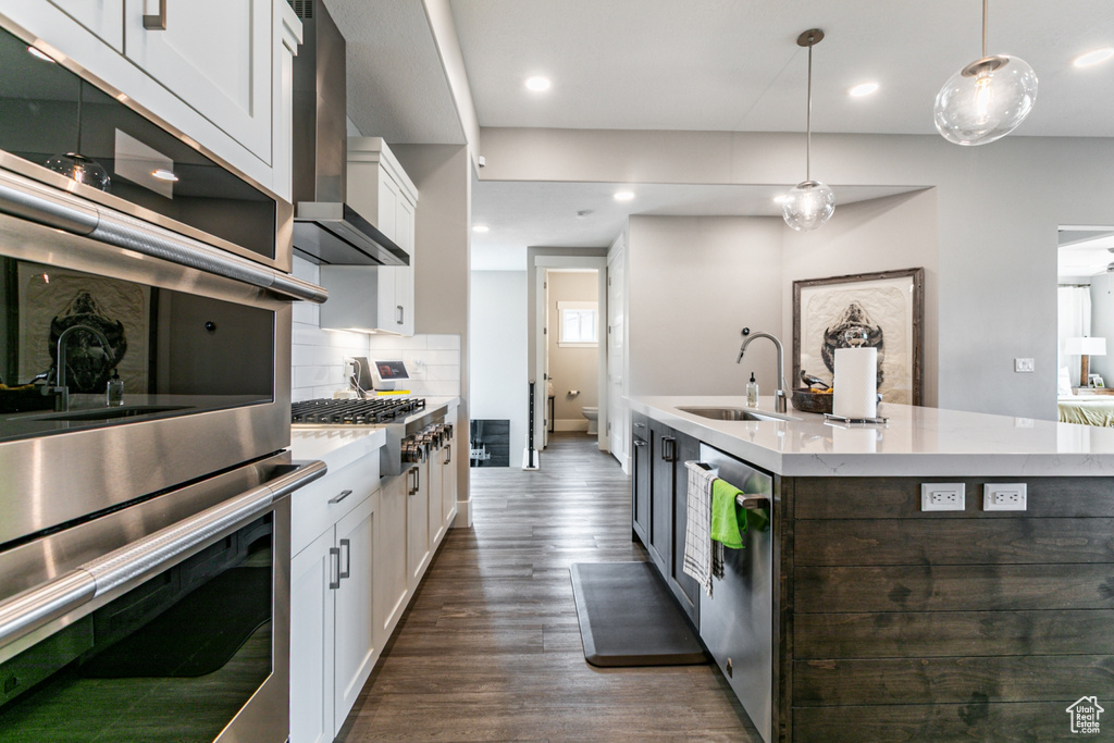 Kitchen with stainless steel appliances, white cabinetry, wall chimney exhaust hood, decorative light fixtures, and recessed lighting