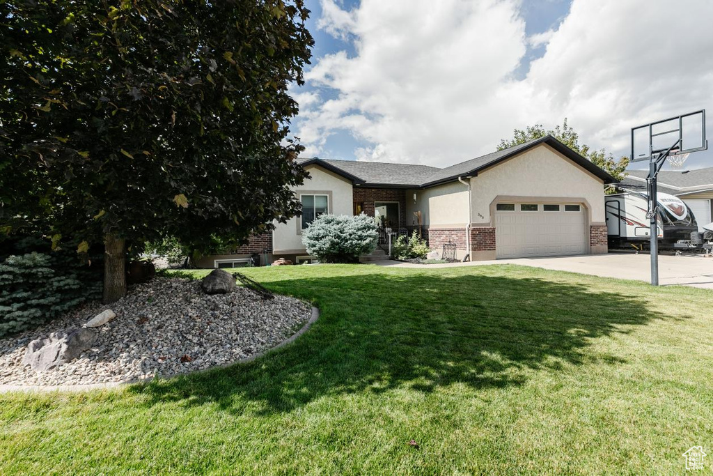 Single story home with a front yard, brick siding, a garage, stucco siding, and driveway