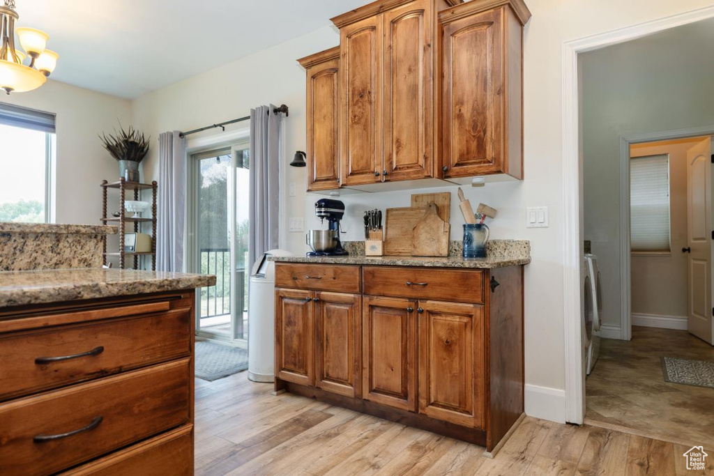 Kitchen featuring light stone counters, brown cabinetry, light wood-style floors, washer / dryer, and a chandelier