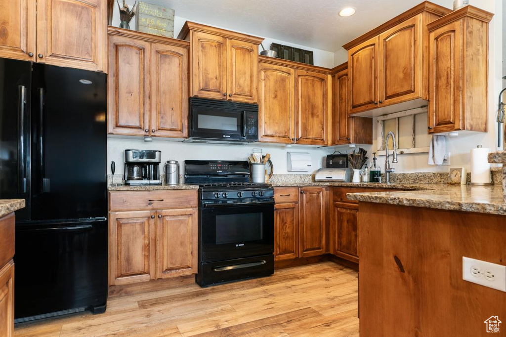 Kitchen featuring black appliances, light stone countertops, light wood-style flooring, brown cabinetry, and recessed lighting
