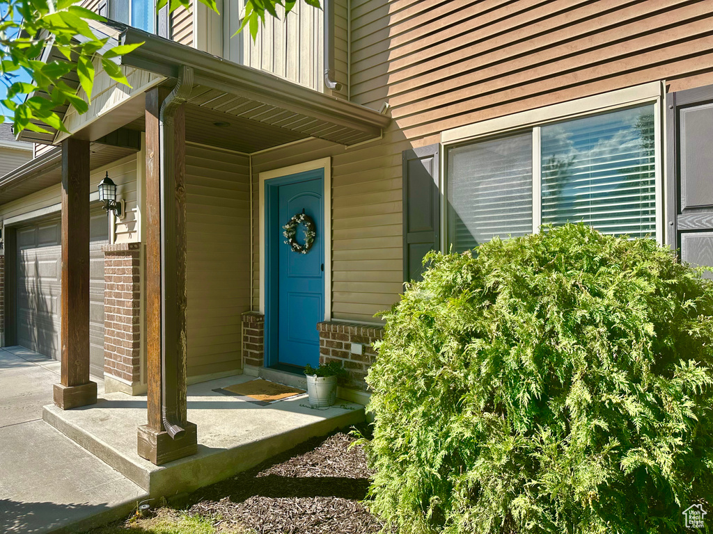 Doorway to property featuring a garage, brick siding, and covered porch
