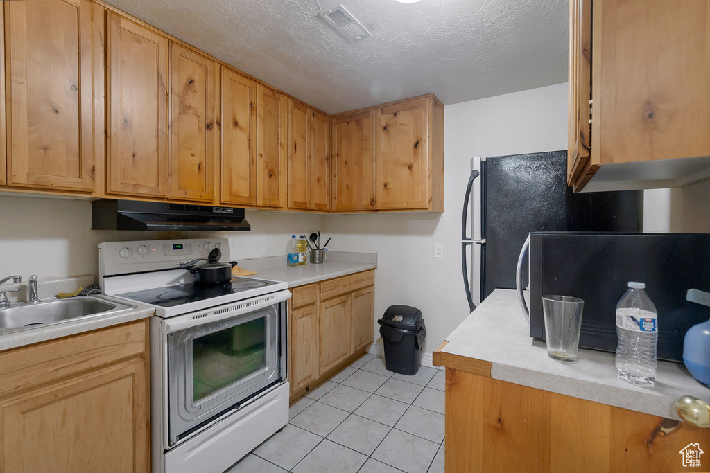 Kitchen with electric range, light tile patterned floors, light countertops, under cabinet range hood, and a textured ceiling