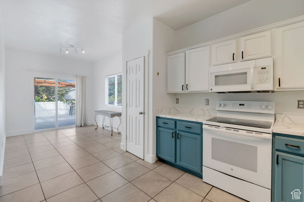 Kitchen featuring white appliances, blue cabinets, white cabinetry, light tile patterned flooring, and light stone counters