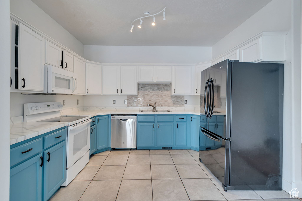Kitchen with blue cabinets, white appliances, white cabinets, light tile patterned floors, and tasteful backsplash