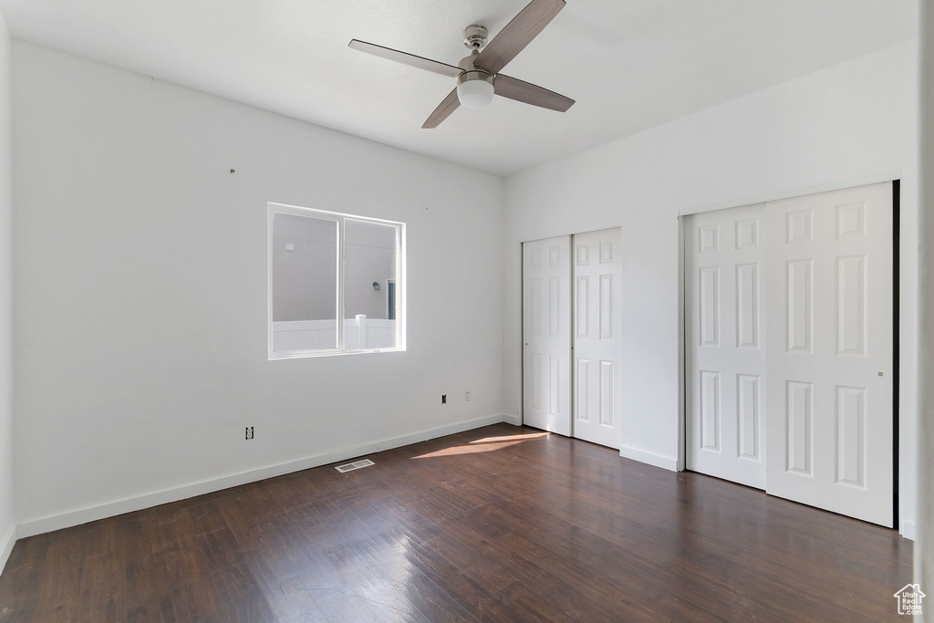 Unfurnished bedroom with two closets, dark wood-type flooring, and a ceiling fan