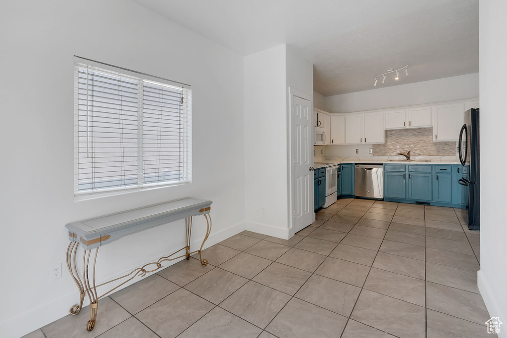 Kitchen with blue cabinets, light tile patterned flooring, white cabinetry, backsplash, and stainless steel dishwasher