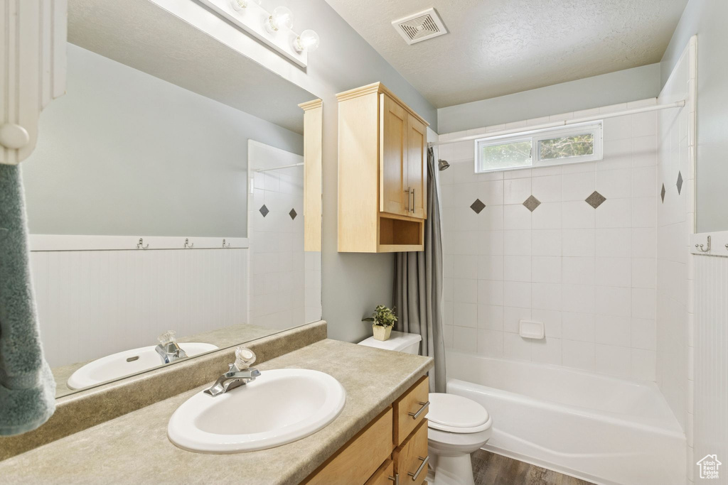 Bathroom featuring shower / bath combo, vanity, a textured ceiling, dark wood-style floors, and a wainscoted wall