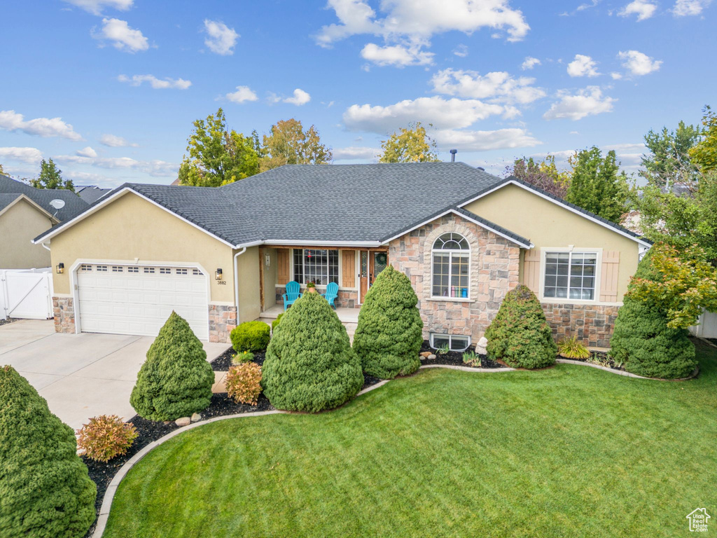 Ranch-style house featuring stone siding, an attached garage, stucco siding, concrete driveway, and a front lawn