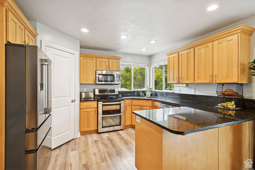 Kitchen with stainless steel appliances, light wood-style floors, a peninsula, recessed lighting, and dark stone countertops