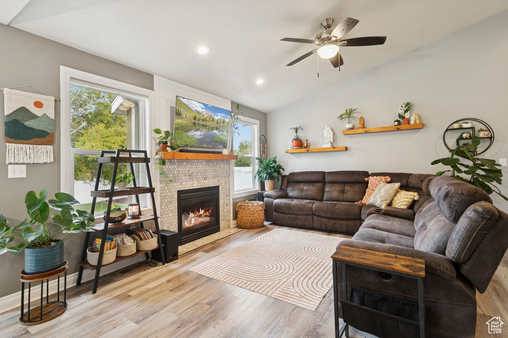 Living room featuring vaulted ceiling, light wood finished floors, recessed lighting, a glass covered fireplace, and a ceiling fan