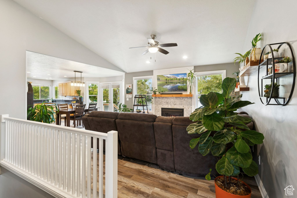 Living room with lofted ceiling, a lit fireplace, wood finished floors, recessed lighting, and ceiling fan