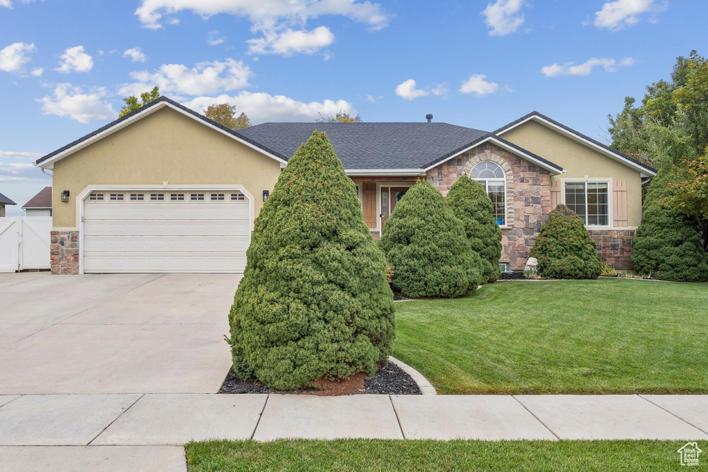 View of front of property featuring stone siding, stucco siding, concrete driveway, and a front yard