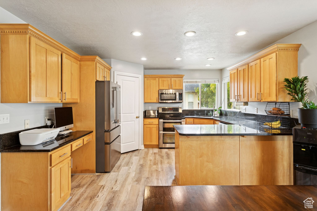 Kitchen with light wood-style flooring, stainless steel appliances, dark stone countertops, recessed lighting, and a peninsula