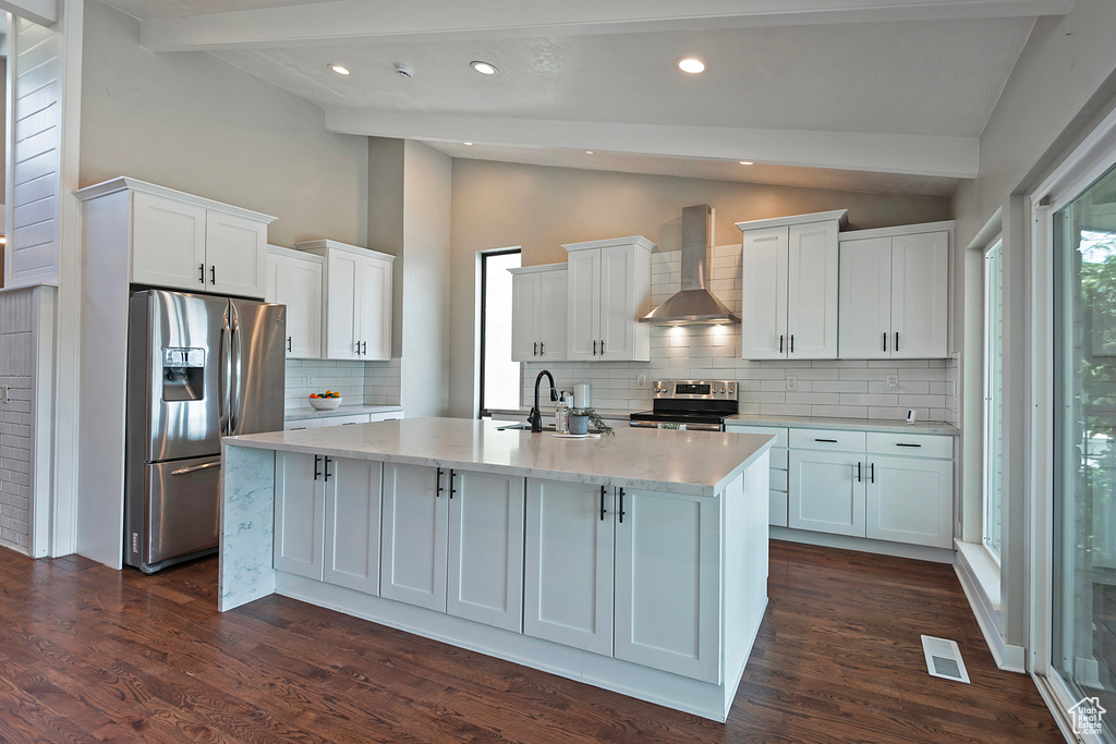 Kitchen with white cabinets, appliances with stainless steel finishes, tasteful backsplash, wall chimney exhaust hood, and light stone countertops