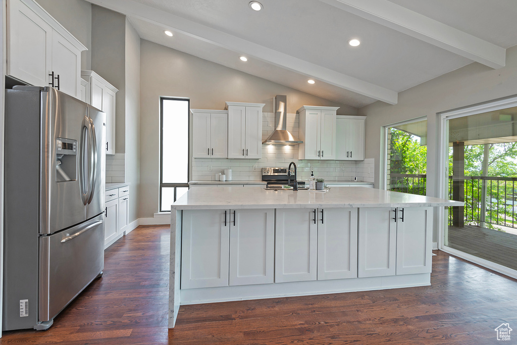 Kitchen with stainless steel appliances, light stone counters, tasteful backsplash, white cabinetry, and wall chimney range hood