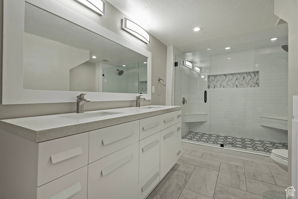 Bathroom featuring a stall shower, double vanity, a textured ceiling, and recessed lighting