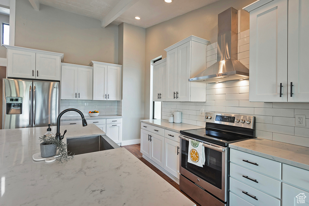 Kitchen featuring stainless steel appliances, wall chimney exhaust hood, white cabinets, light stone counters, and tasteful backsplash