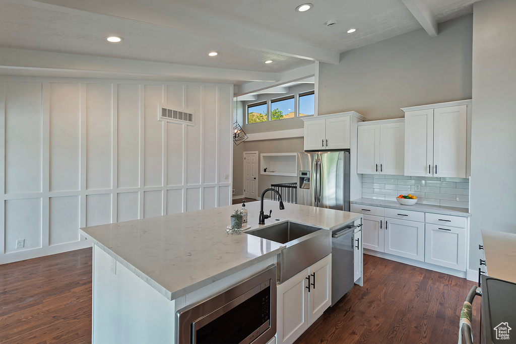 Kitchen with white cabinets, a kitchen island with sink, appliances with stainless steel finishes, dark wood-style floors, and beam ceiling