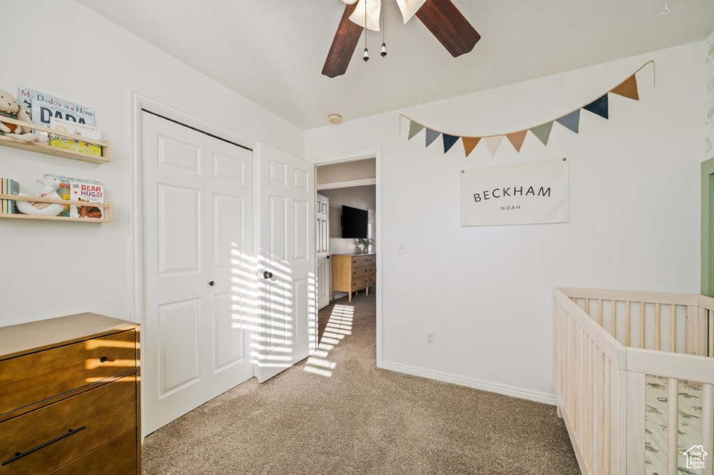 Unfurnished bedroom featuring light colored carpet, a crib, and ceiling fan