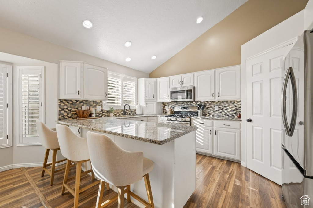 Kitchen with lofted ceiling, white cabinetry, light stone countertops, tasteful backsplash, and a kitchen breakfast bar