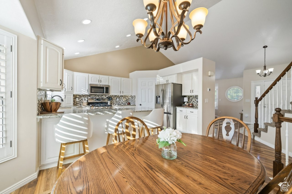 Dining space with lofted ceiling, stairway, a chandelier, and light wood-style flooring