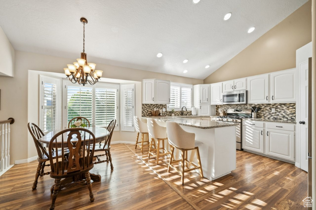 Kitchen featuring backsplash, a breakfast bar, dark stone counters, white cabinets, and hanging light fixtures
