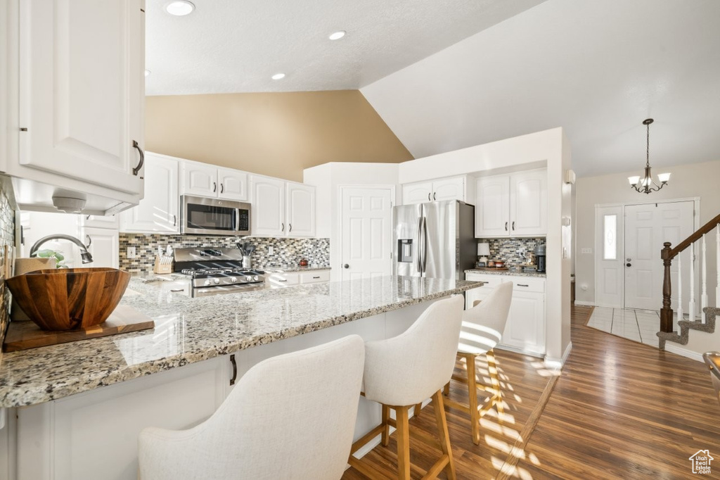 Kitchen with tasteful backsplash, light stone counters, dark wood-type flooring, lofted ceiling, and a kitchen breakfast bar