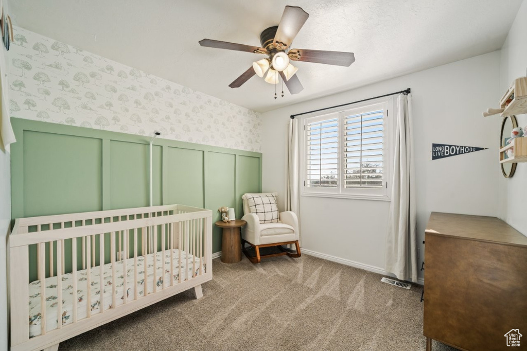 Carpeted bedroom featuring a crib and a ceiling fan