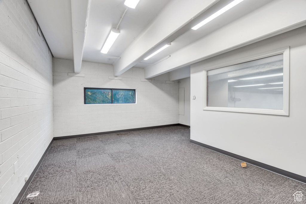 Carpeted empty room with brick wall and beam ceiling