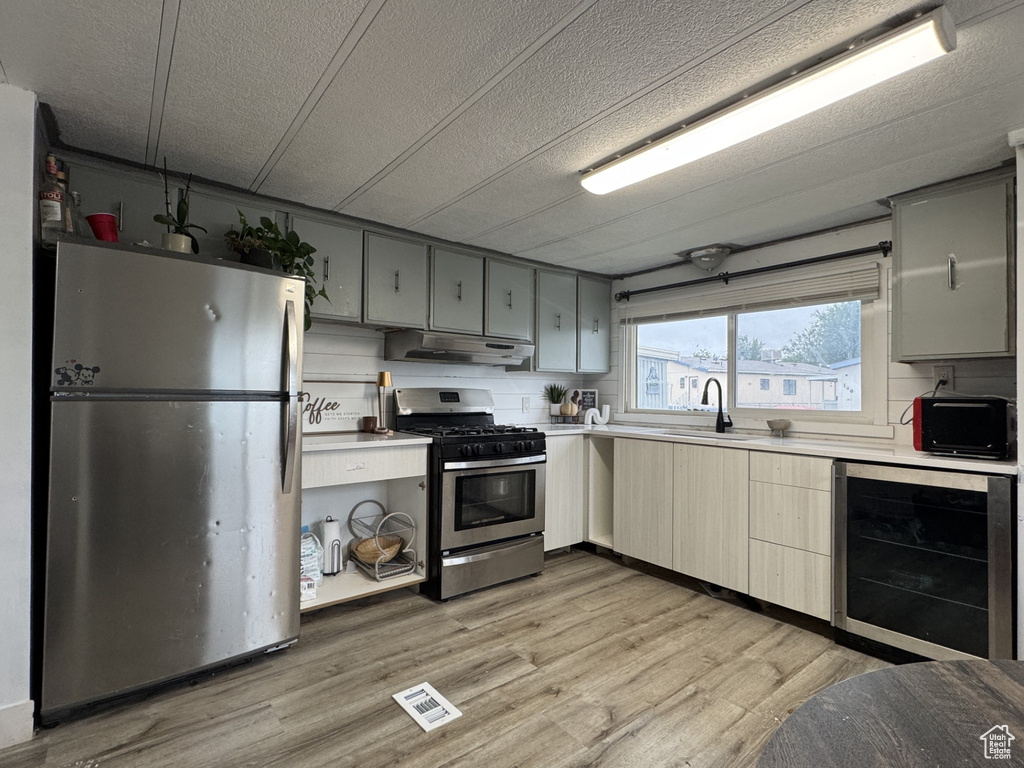Kitchen featuring appliances with stainless steel finishes, light countertops, beverage cooler, light wood finished floors, and under cabinet range hood