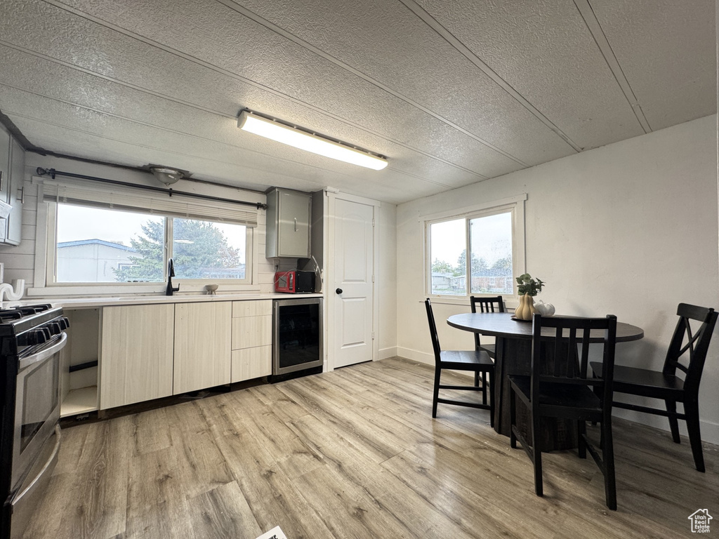 Kitchen featuring light brown cabinetry, beverage cooler, stainless steel stove, light wood finished floors, and a textured ceiling