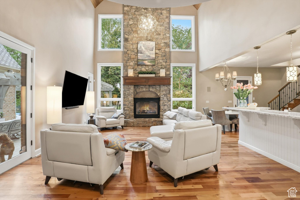 Living room featuring a stone fireplace, stairway, light wood-style floors, healthy amount of natural light, and a high ceiling
